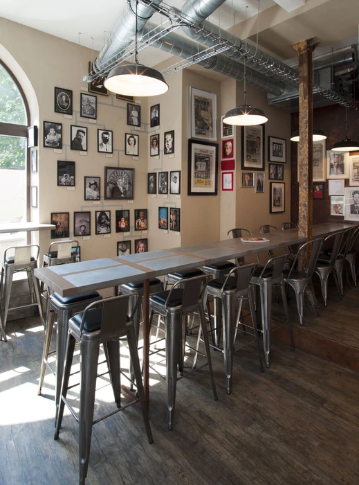 Intérieur industriel-chic d'un bar-restaurant avec une longue table haute en bois massif entourée de tabourets Tolix en métal brossé avec assises rembourrées