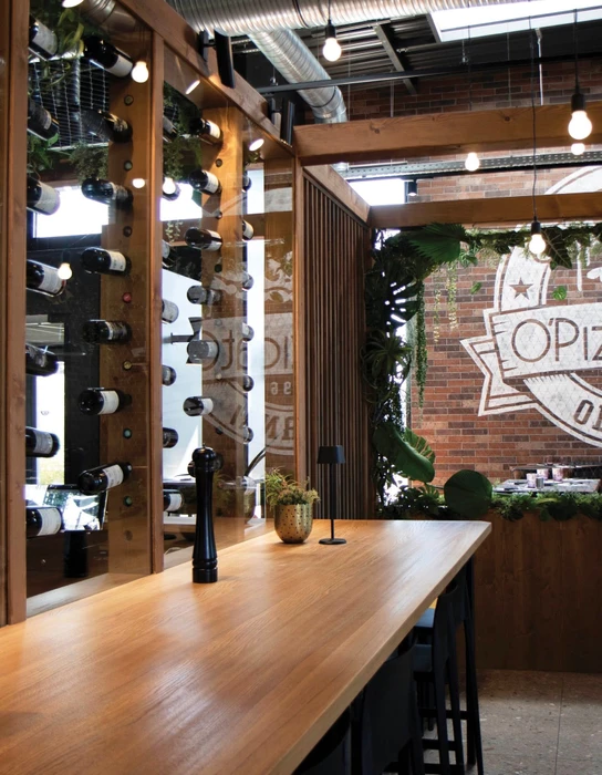 Intérieur d'un restaurant tendance avec bar en bois massif, casier à vins mural en métal et bois exposant des bouteilles horizontalement