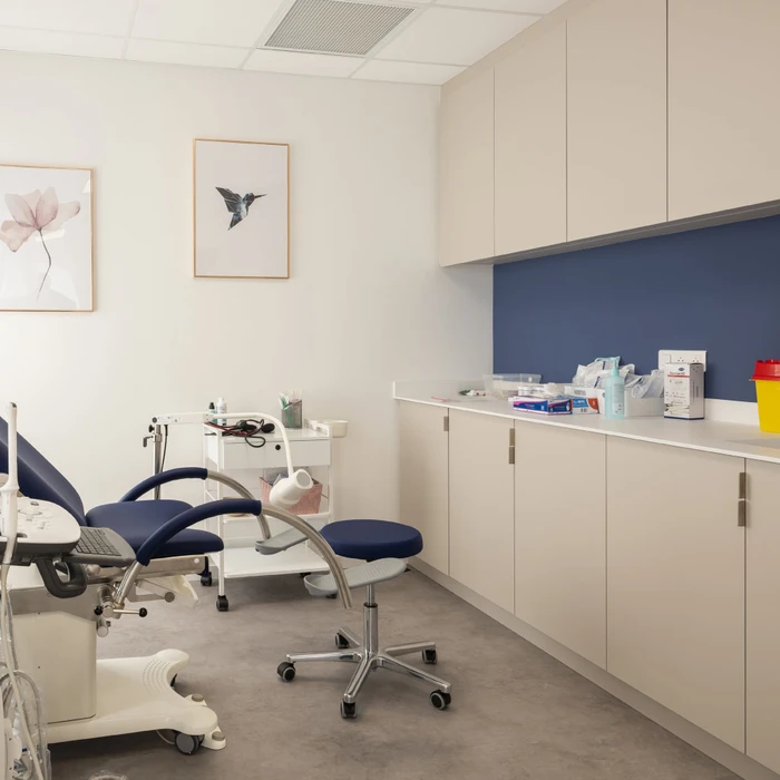 Cabinet médical moderne avec fauteuil d'examen ergonomique en similicuir bleu marine, tabouret assorti et colonne médicale sur roulettes
