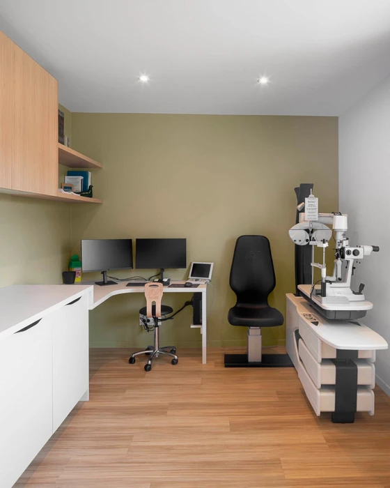 Cabinet d'ophtalmologie moderne, salle d'examen équipée d'une lampe à fente, unité de réfraction sur table motorisée, deux moniteurs sur bras articulé, tablette tactile