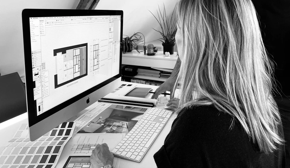 Architecte ou designer travaillant à son bureau dans un atelier sous combles, analysant un plan d'étage sur iMac Apple